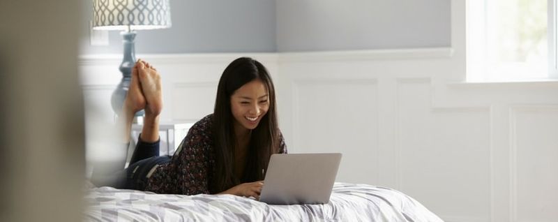 girl smiling in bed while using laptop