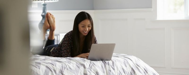 woman lying on bed and using laptop - SingSaver